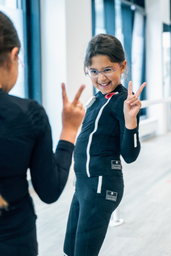 Exopulse Suit kids Kleines Mädchen im Exopulse Suit Kids posiert lebensfroh vor einem Spiegel, Münch & Hahn Sanitätshaus