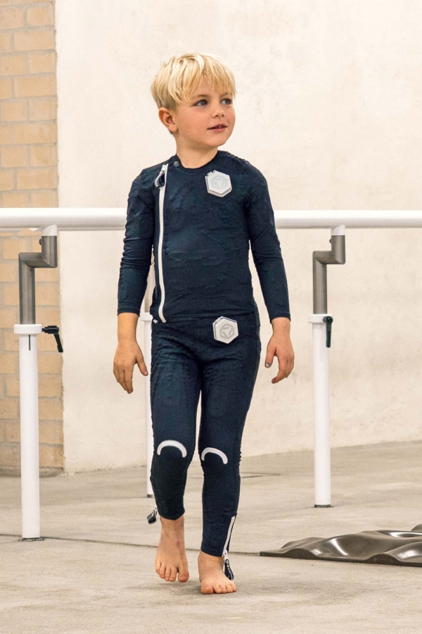 Exopulse Suit Otto 1 Kleiner Junge mit neurologischer Erkrankung steht im Exopulse Suit kids bei Münch & Hahn Sanitätshaus